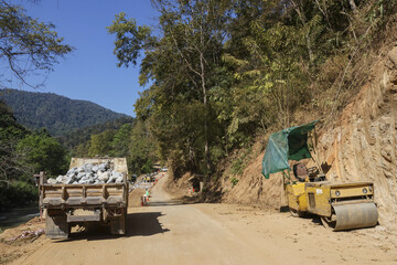 Dump truck and road roller on dirt road at construction site in rural mountain landscape. scene showing progress and infrastructure development in remote area © CoreRock