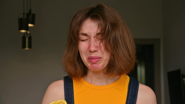 A young Caucasian woman bites into a fresh lemon, enjoying its tart taste. Her face twists from the citric acid. Homemade shot in the kitchen.