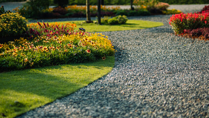 Fototapeta premium Beautiful landscape garden with winding gravel path and colorful flowers in morning sunlight