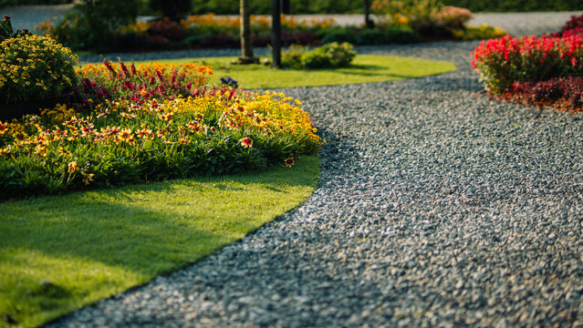 Beautiful landscape garden with winding gravel path and colorful flowers in morning sunlight
