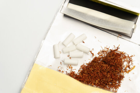 Rolling tobacco, cigarette filters, and thin papers scattered on a white background, representing smoking habits and addiction