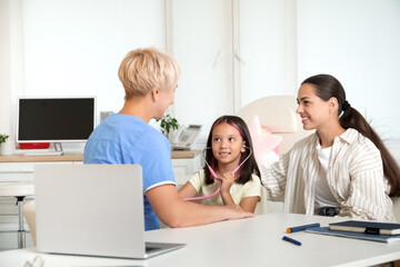 Fototapeta premium Little Asian girl with stethoscope listening to pediatrician and mother in clinic
