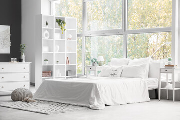 Big comfortable bed, chest of drawers, shelving unit and bedside table in interior of bedroom