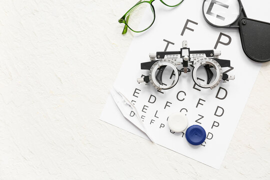 Optical trial frame with eye test chart, eyeglasses and set for contact lenses on white grunge background