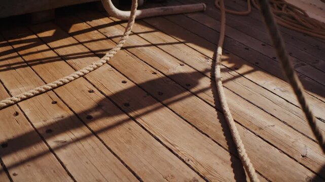 Close-up of sailing ropes and shadows on wooden deck, warm sunlight creating patterns across planks, nautical detail and maritime atmosphere concept.