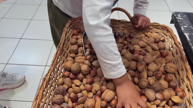 close-up view of the hands of a playful 5-year-old black kid playing with assorted nuts in a basket. slow motion shot.