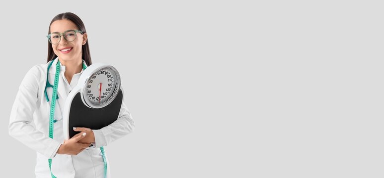 Female nutritionist holding weight scales on light background with space for text