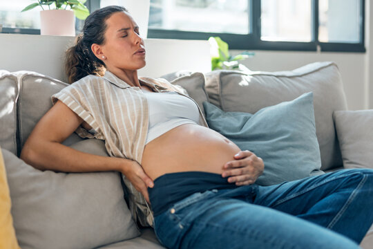 Pregnant woman with back pain and sciatica sitting on the couch at home