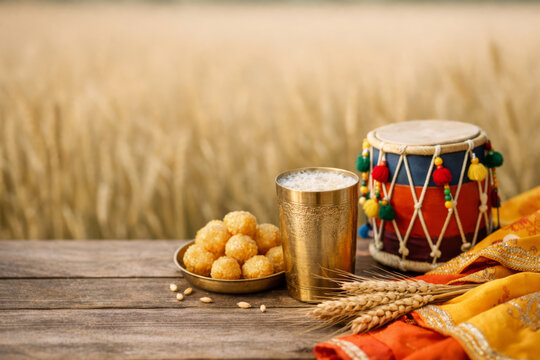 Vaisakhi harvest festival concept featuring Punjabi culture symbols, food and dhol on blurred wheat farm.