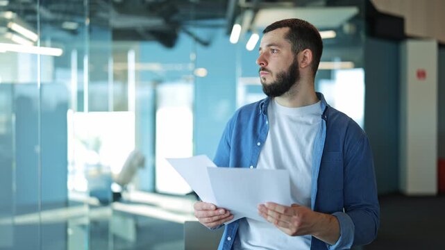 Thoughtful man in a contemporary office space, meticulously reviewing important business documents. His focused expression conveys dedication and careful consideration of details.