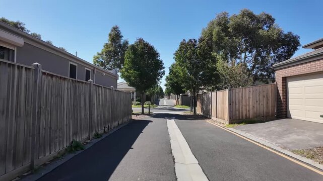 A narrow residential laneway or back street in an Australian suburban neighborhood, lined with timber fencing and private garage access. Suburban living, residential boundary and fencing.