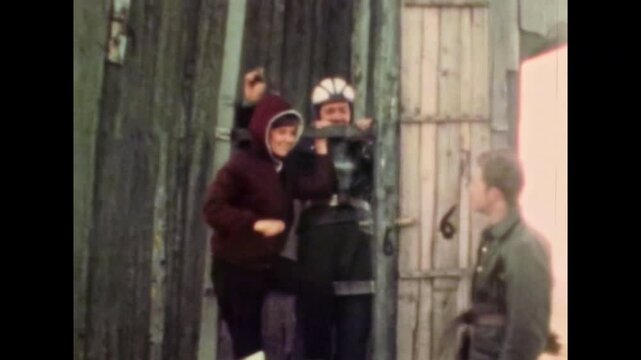 Young friends posing near wooden windmill, barn in rural countryside. Friendship at outdoor joint leisure. People exploring rural destinations together. Old film. Archival retro. Vintage archive