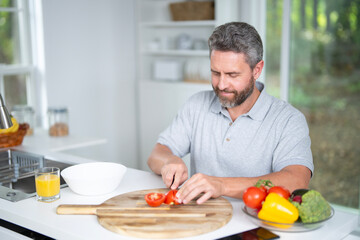 Fototapeta premium Man eats breakfast in the kitchen on morning. Man enjoys a healthy meal at the kitchen table. A man eats cereal and fruit in the kitchen during morning hours. Man eats vegetables for lunch.