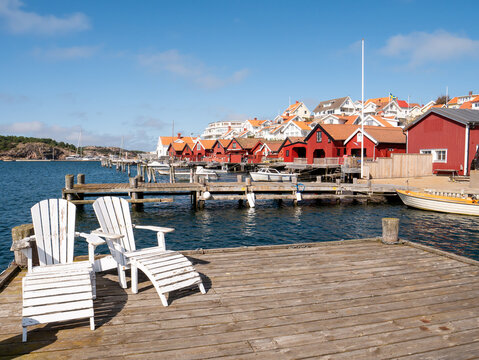 Wooden pier with white adirondack chairs and red boathouses in Fj&auml;llbacka, Bohusl&auml;n, V&auml;stra G&ouml;taland, west coast Sweden