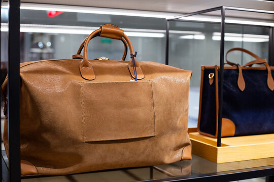 Leather brown travel bag on store shelf. Choosing right bag for long trip. Buying useful and stylish handbag at luggage store. Purchase suitcase for trip. Commercial store selling travel supplies
