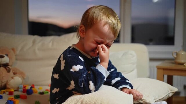 Petit gar&ccedil;on blond pleurant doucement sur son oreiller avec ses jouets