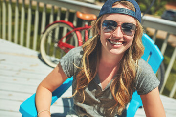 Relax, smile and portrait with woman outdoor in sunglasses, summer vacation and weekend break. Happiness, eyewear and peace with female person on deck chair of home for calm and holiday trip