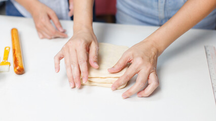 Fototapeta premium Closeup hand of woman bakers preparing knead dough with butter on white table counter process making pastry pie workflow ingredients flour homemade sweet dessert bread baking cooking in bakery kitchen