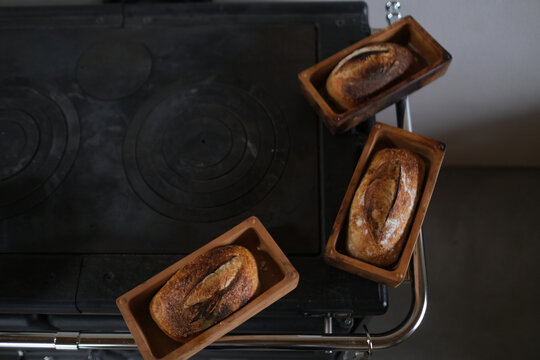 Three Rustic Sourdough Loaves in Wooden Baskets on a Dark Stove Top