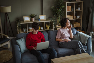 Obraz premium Mother and teenage son using devices on sofa