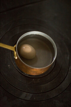 Single brown egg boiling in a copper pot on a dark stovetop