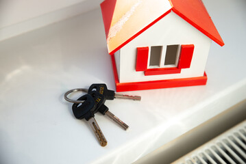 Keys beside redwhite model house on windowsill, sunlight glint on metal, symbolic purchase and movein readiness, contract