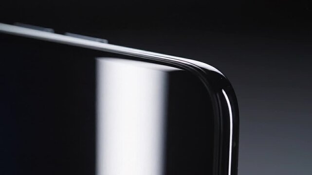 Extreme close-up shot revealing the seamless curvature of a highly reflective black smartphone screen edge, emphasizing premium material and modern technological design against a minimalist dark backg