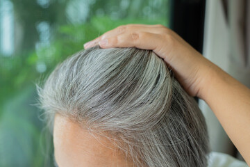 Fototapeta premium Woman showing gray hair and roots while touching her head with her hand.