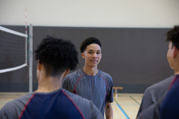 African American teenage males practicing on gym volleyball court, wearing gray shirts near net