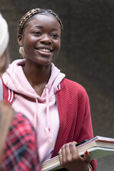 African American teenage female and peer smiling, holding books at school, wearing red jacket