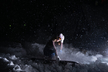 A girl snowboarder sitting in the snow at night