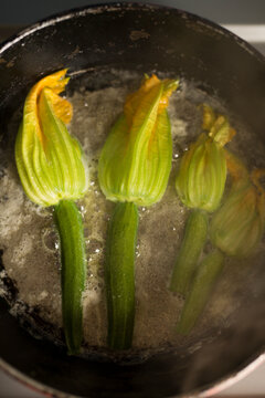 Sizzling young zucchini with blossoms being fried in a pan