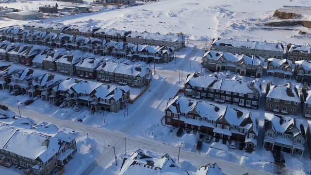 Aerial drone view of new housing development in Erin Ontario, showing rows of modern townhouses, snow covered streets, residential neighborhood layout, and growing suburban community