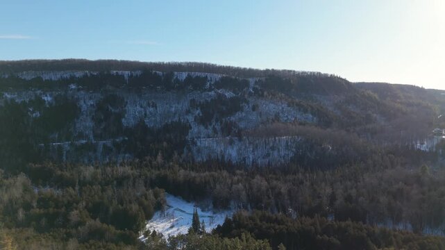 Aerial drone view of Devils Pulpit mountain in Forks Of The Credit, Caledon Ontario with Credit River in foreground, forested slopes, winter landscape and scenic natural surroundings near Toronto