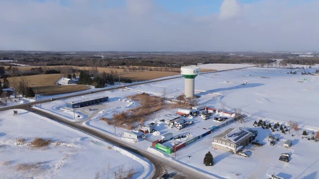 Aerial drone shot of water tower surrounded by snow covered rural landscape in Erin, Ontario, Canada, highlighting winter fields, roads, and small town infrastructure