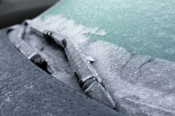 Closeup of an icy windshield with frozen wiper blades, showcasing winter weather conditions and cold temperature challenges for vehicles.