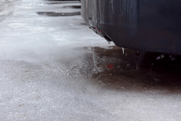Rear view of a vehicle emitting exhaust over a frozen, icy road surface in winter. Clear focus on ice texture and cold conditions.