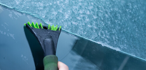 Close-up of a green ice scraper removing frost from a car windshield on a cold winter day, with clear detail and strong color contrast.