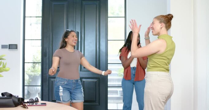 Diverse women friends greeting arriving woman entering front door, celebrating visit by entry table