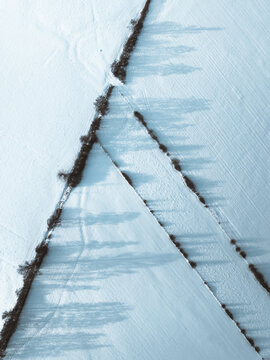 Aerial view of a snowy expanse bisected by dark lines of trees casting long shadows on the pristine white landscape, Dabo, Grand Est, France.