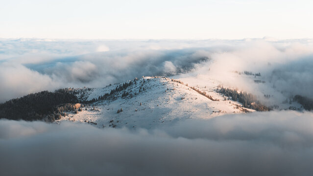 View of a snow-dusted mountain peak piercing through a sea of cotton-like clouds, bathed in the soft glow of the sun, Stosswihr, Grand Est, France.