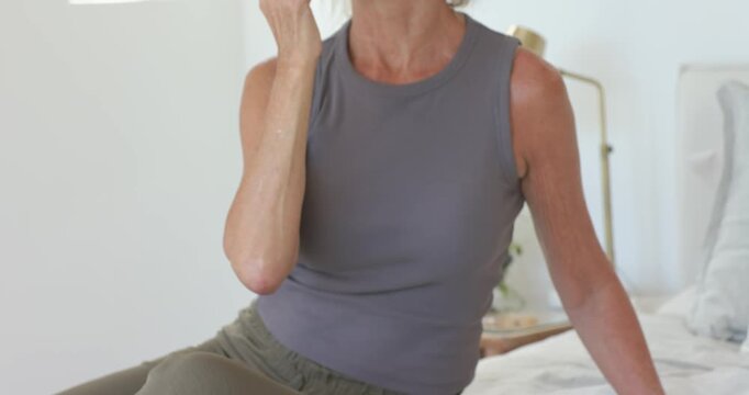 Senior female on bed seeing skincare towel reaching for pink roller massaging jaw for skincare