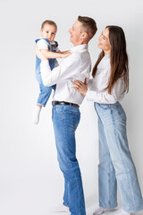 United Positive Young Smiling Happy Caucasian Parents Mom and Dad With Little Son Child Kid Boy Wearing Casual Jeans Clothing Gladly Together Hugging as Traditional Family Relationships Concepts.