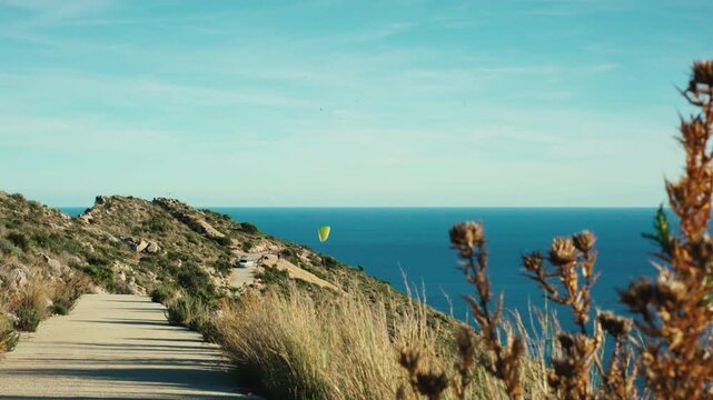 Scenic coastal landscape with paraglider overlooking ocean and rocky pathway