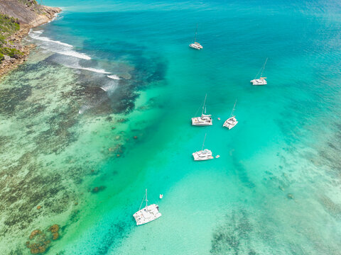 Aerial view of boats scattered across the turquoise water along the coast, a tropical paradise unveiled from above, Baie Ste Anne, Seychelles.