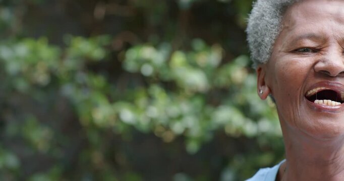 Senior African woman smiling, laughing as camera moving, reacting to prompt near hedge, copy space
