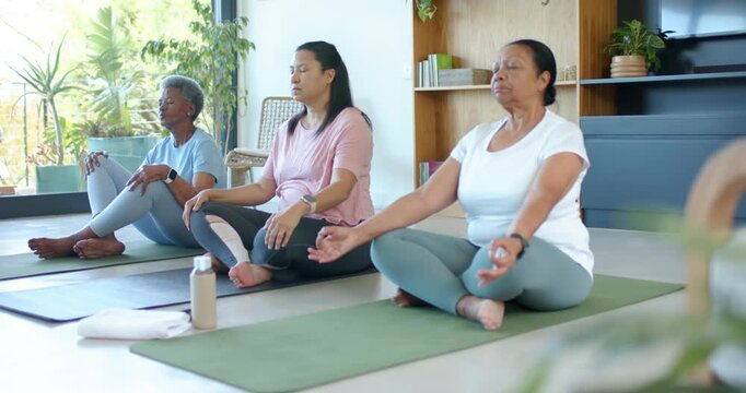 Diverse women following guided cue in studio, sitting on mats holding mudras with bottle and towel