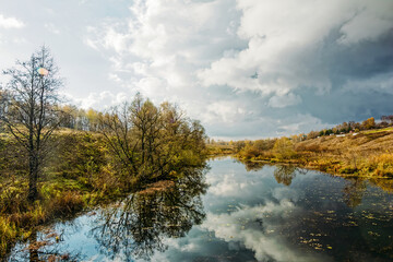 Fototapeta premium A small river near a village on a cloudy autumn day
