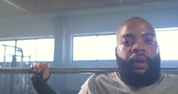 African American man bracing, spotter placing barbell across shoulders in gym preparing squat