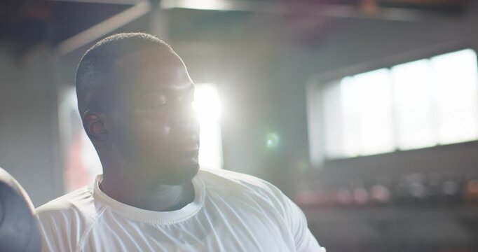 African American man turning head toward camera in loft-gym wearing white tee, reacting to flare